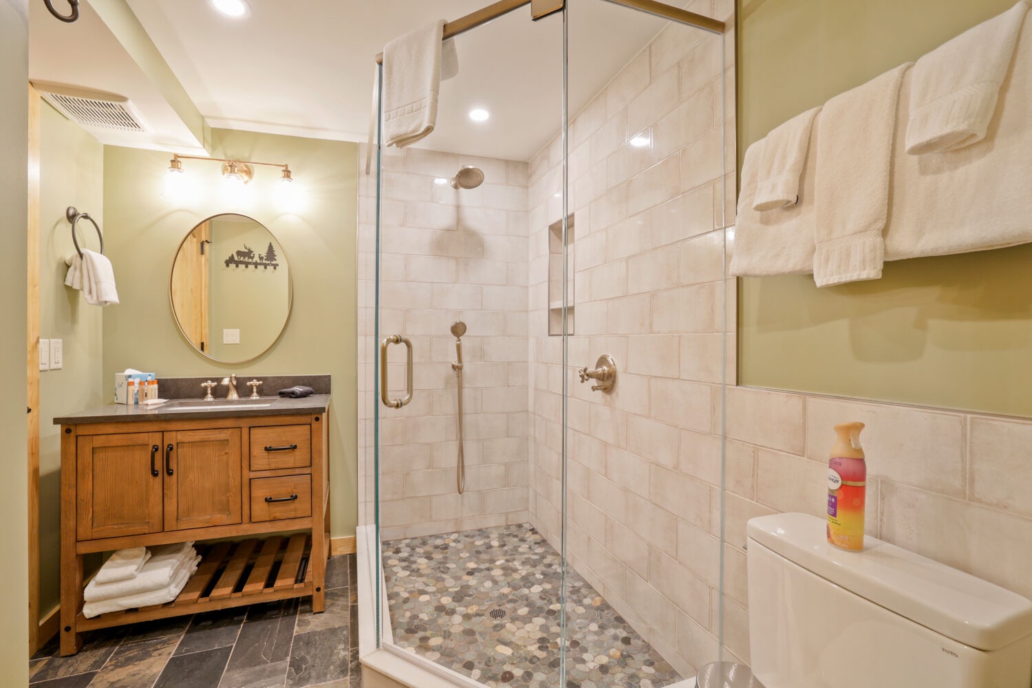 Step into your spa-like bathroom featuring a spacious walk-in shower with rainfall showerhead, elegant pebble flooring, and warm natural wood vanity stocked with plush towels for your comfort.