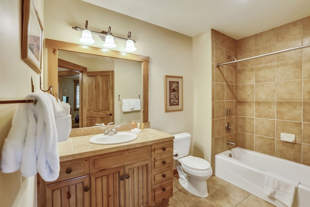Unwind in your elegant bathroom featuring warm wood vanity, luxurious tiled tub-shower combo, and thoughtful amenities for ultimate comfort.