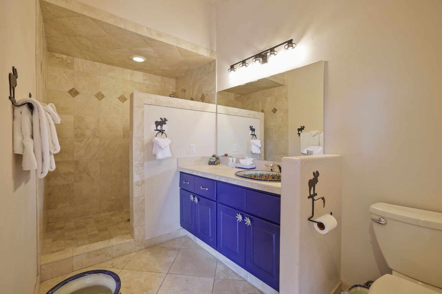 Refresh in your spacious bathroom with a walk-in shower, vibrant cabinetry, and soft robes waiting for you after a long day exploring.