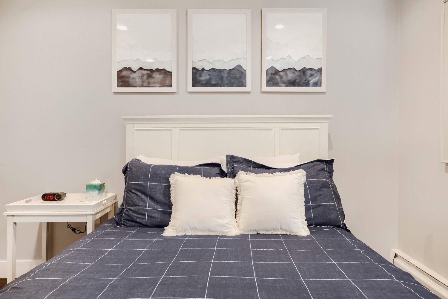 Sink into plush bedding beneath soothing mountain artwork in your peaceful retreat. This serene bedroom invites restful nights with its calming palette and cozy linens.