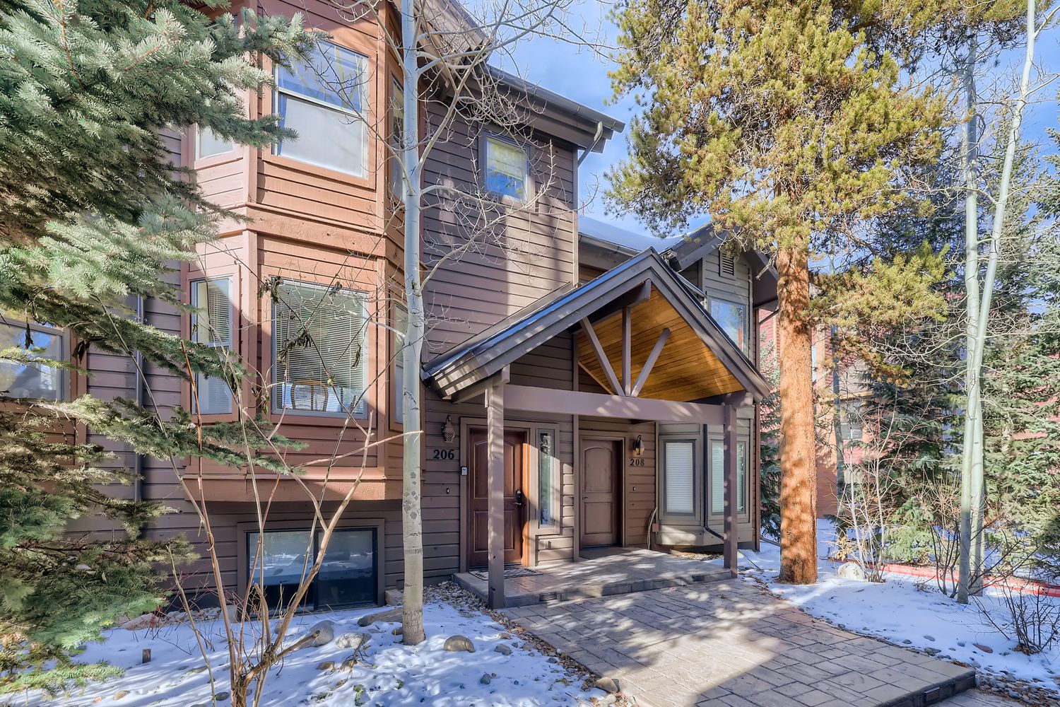 Modern mountain lodge with distinctive timber architecture nestled among evergreen trees, featuring covered entry and winter seasonal charm.