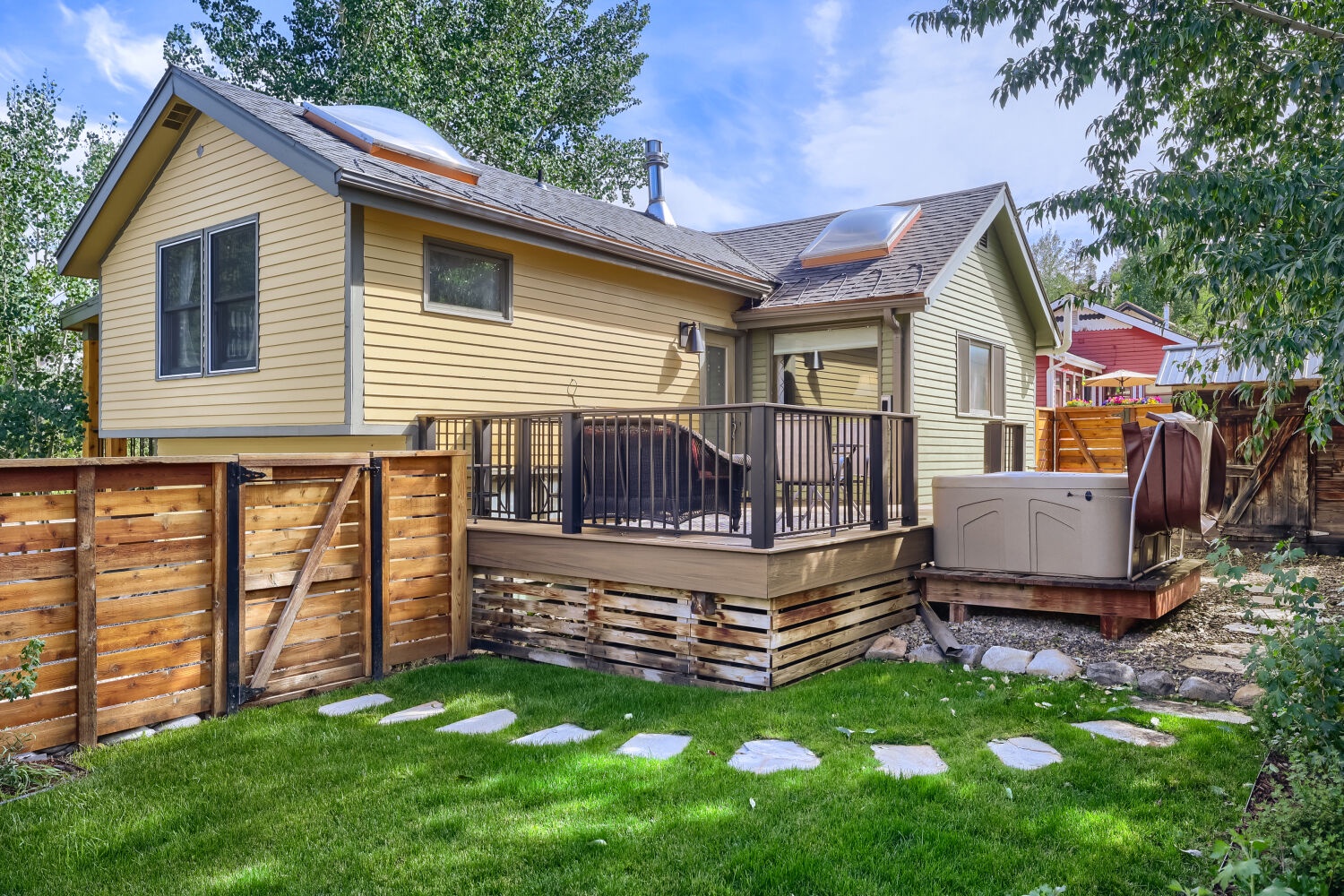 A cheerful yellow home awaits in a quiet neighborhood, complete with a private deck and hot tub nestled among leafy trees and a well-kept lawn.