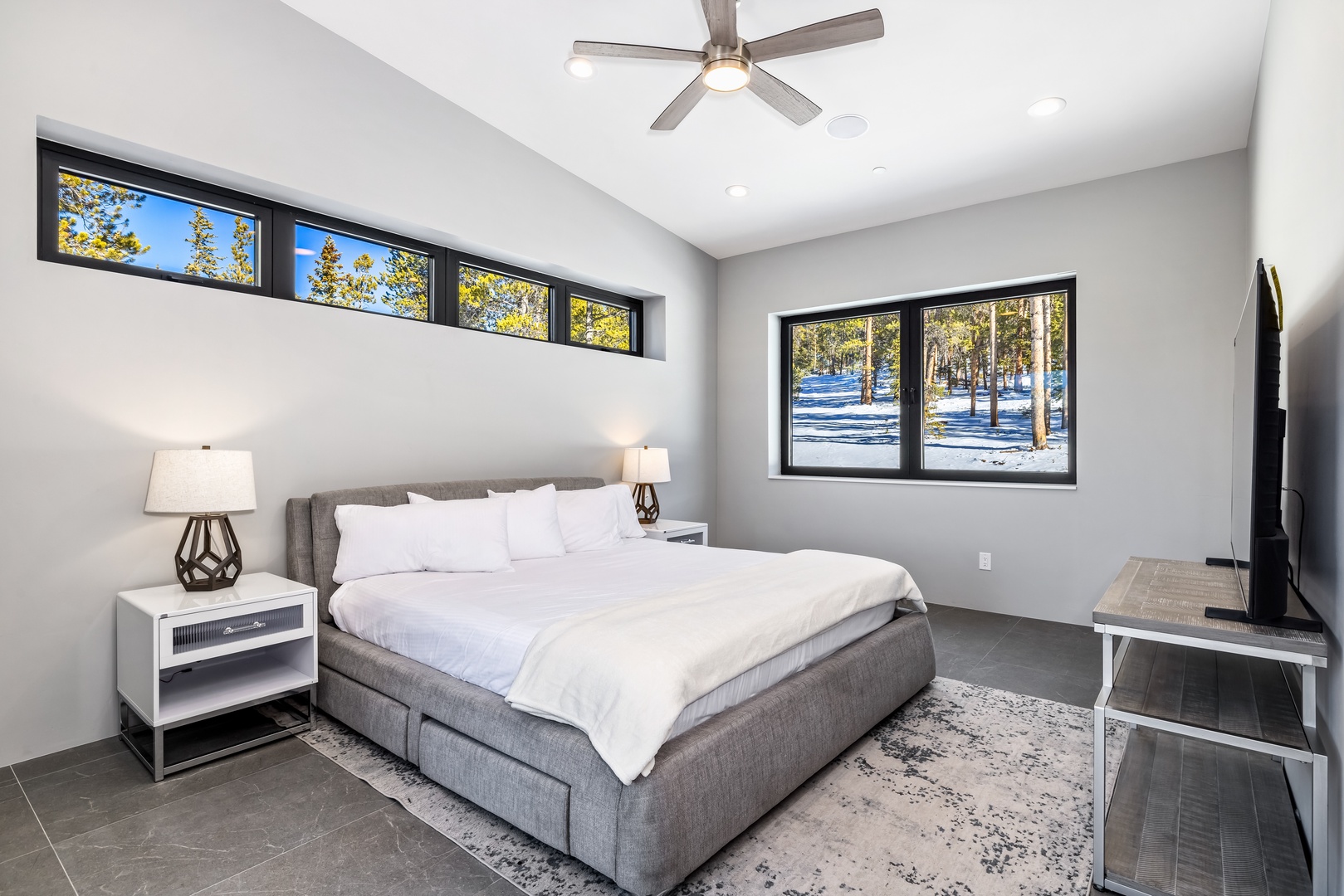 Drift off in your modern bedroom sanctuary with crisp linens, natural light, and peaceful winter views through expansive windows.