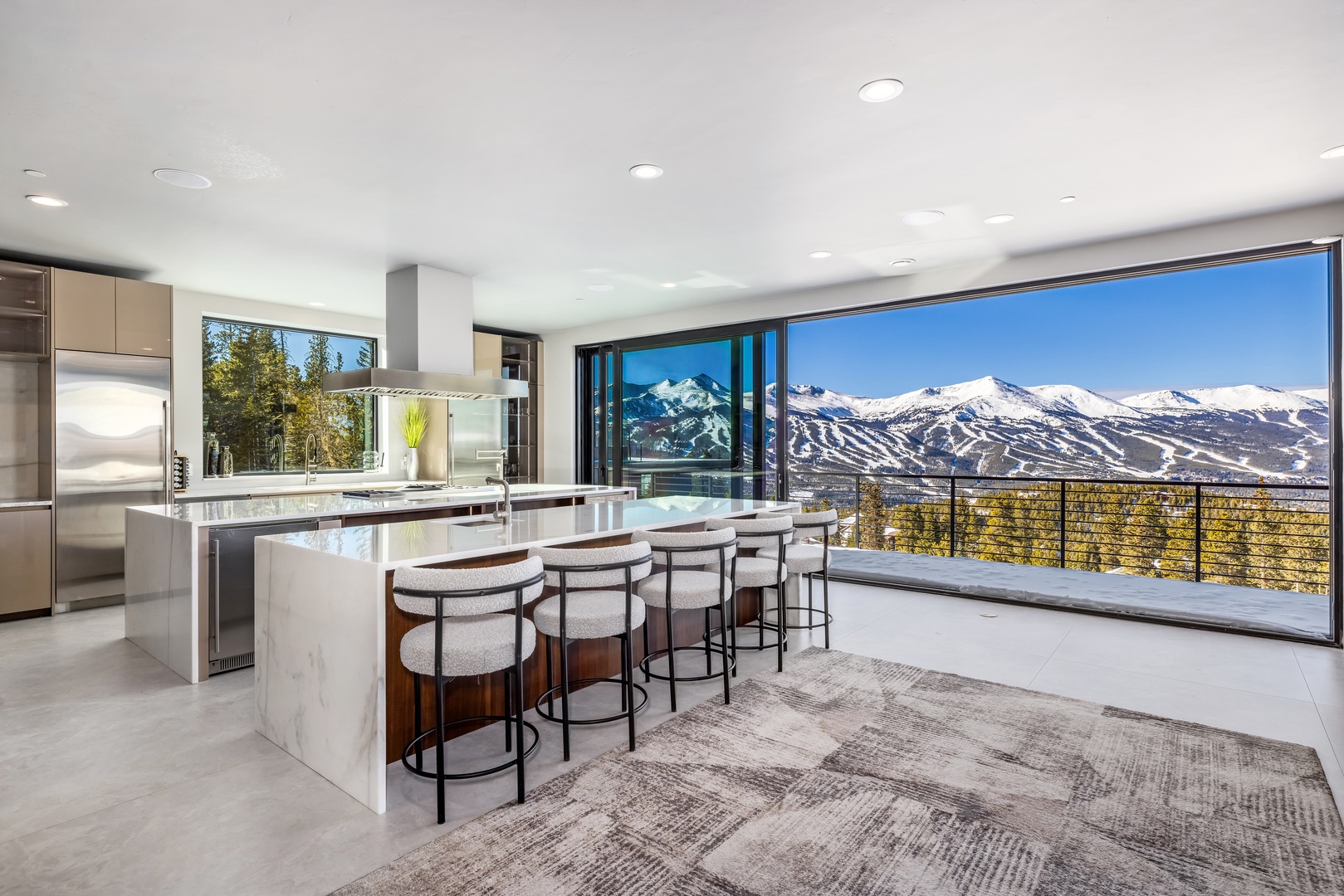 Your modern kitchen features sleek marble countertops and bar seating, perfectly framed by floor-to-ceiling windows showcasing breathtaking mountain vistas.