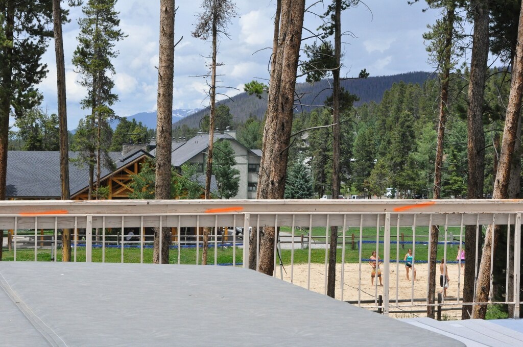 Forested mountain setting with recreational facilities including beach volleyball courts surrounded by tall pine trees.