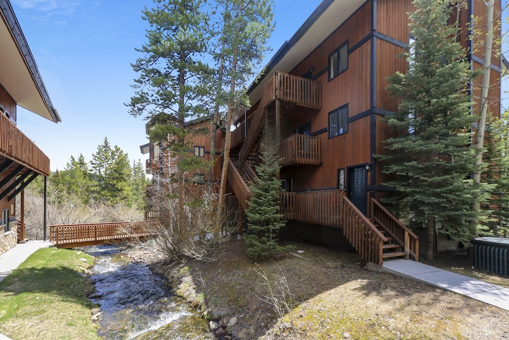 Multi-level mountain lodge with wooden balconies overlooks a peaceful creek, surrounded by towering pines and natural alpine beauty.