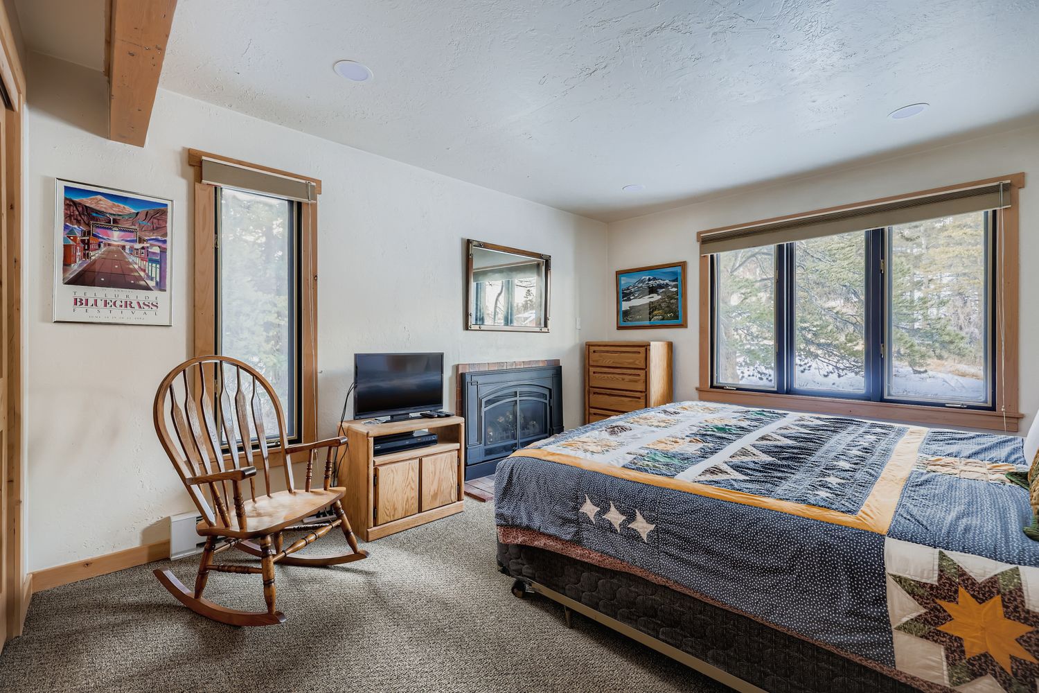 Relax in your cozy bedroom featuring rustic charm with wood accents, a fireplace, and peaceful views through large windows.