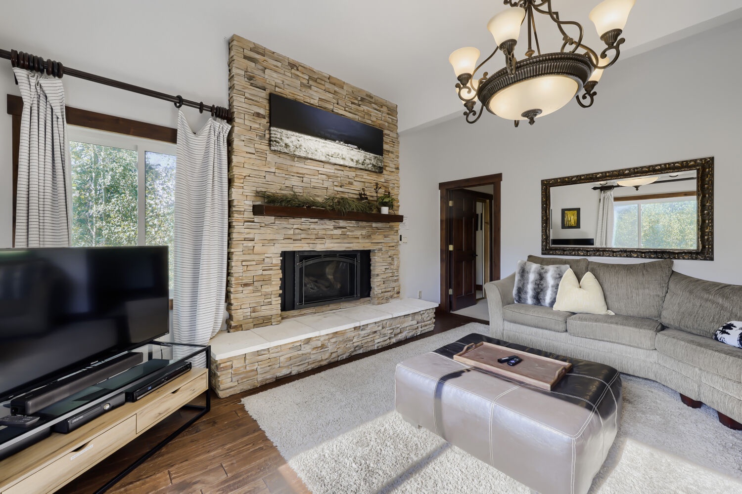 Curl up in this inviting living room, where warm wood floors, a cozy stone fireplace, and natural light create the perfect retreat for your downtime.
