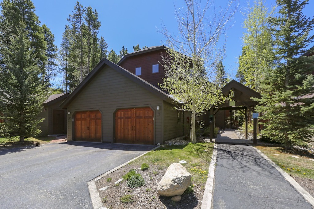 Modern mountain retreat nestled among towering pines with spacious driveway and natural stone landscaping for peaceful arrival.