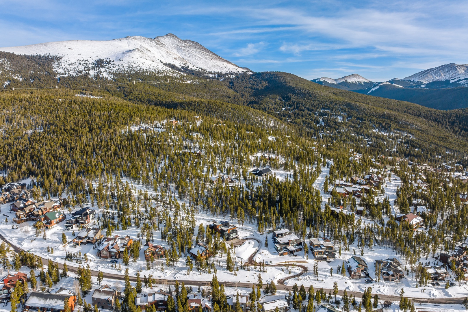 Aerial view of mountain resort community nestled among snow-covered peaks and evergreen forests, showcasing the pristine winter landscape surrounding the property area.