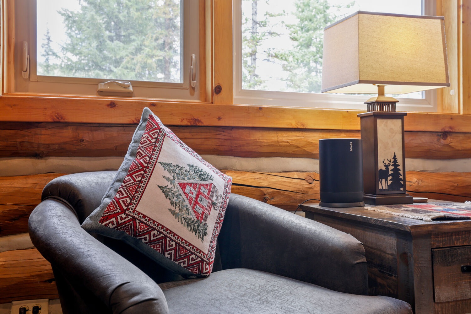 Curl up in a cozy armchair by the window, where rustic wooden walls and mountain air create your perfect retreat. A handcrafted lamp and personal touches make this spot ideal for sipping coffee and soaking in the peaceful, natural surroundings.