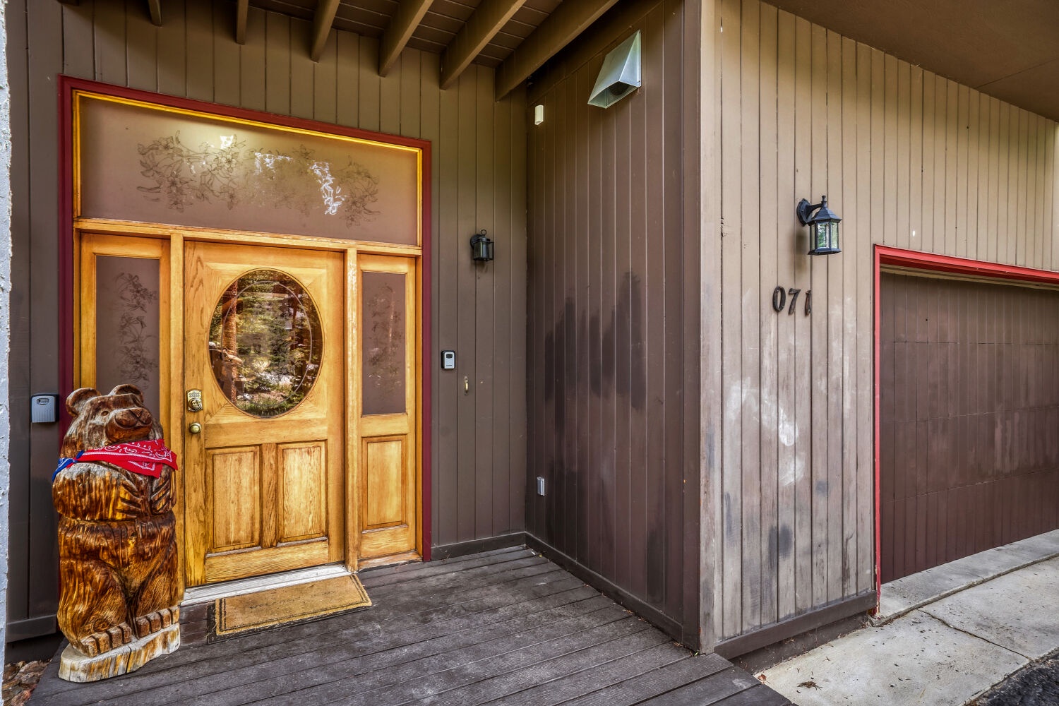 A charming cabin entrance welcomes you with rustic wood paneling, warm lighting, and a friendly carved bear statue greeting guests at the door.