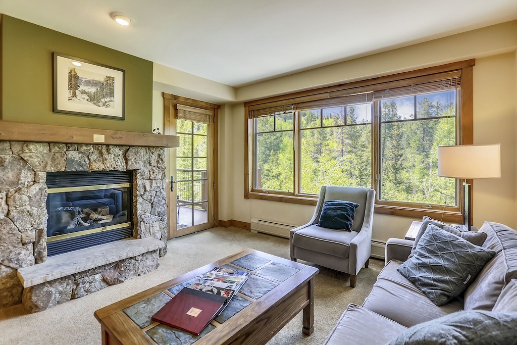 Unwind by your cozy stone fireplace while gazing at forest views through expansive windows in this serene living room retreat.