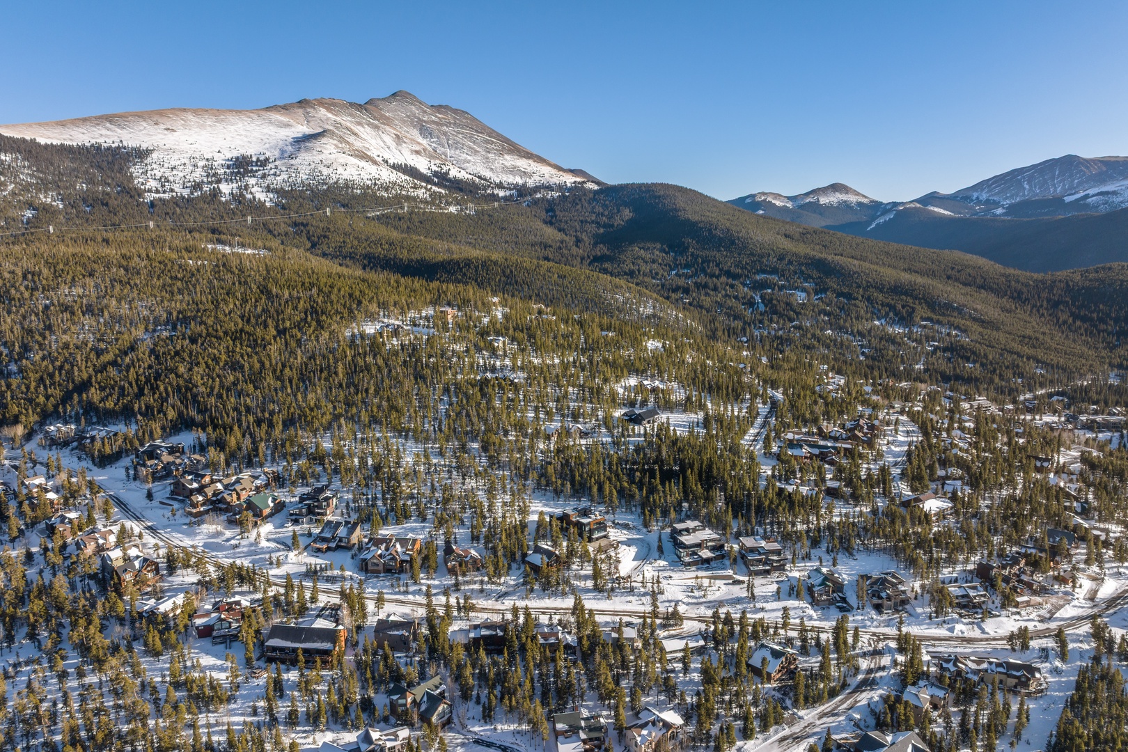 Stunning aerial view of a mountain resort town nestled among snow-covered peaks and forested valleys during winter.