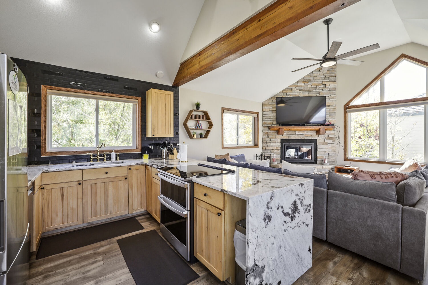 Step into your cozy mountain retreat where natural wood beams soar above an open-concept living space. The gleaming kitchen flows into a welcoming lounge area, all warmed by a stunning stone fireplace—your perfect home base for relaxation.