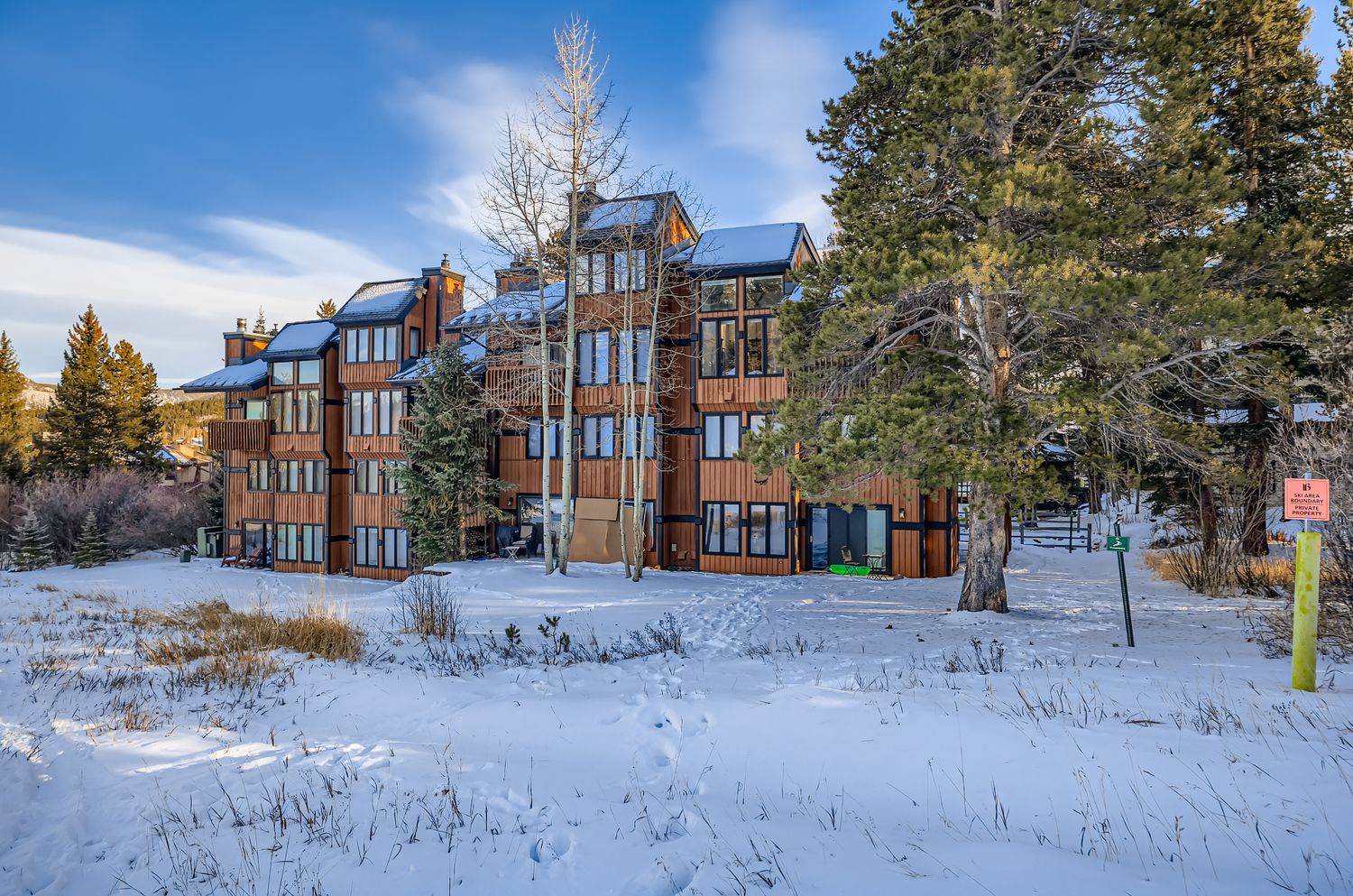 Modern mountain lodge nestled in snow-covered landscape with towering evergreens and crisp winter air.