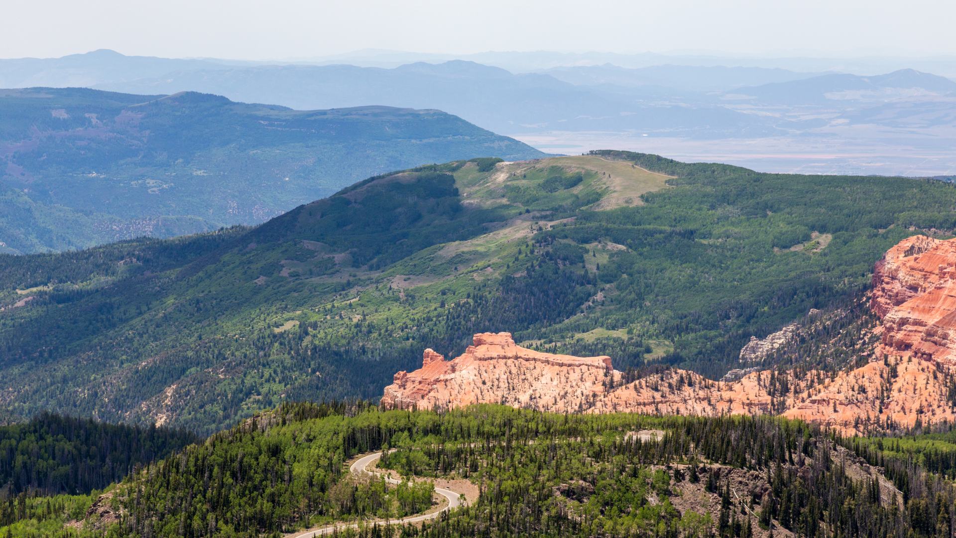 Sweeping panorama of layered mountain ranges, pine forests, and striking red rock formations in the surrounding wilderness area.