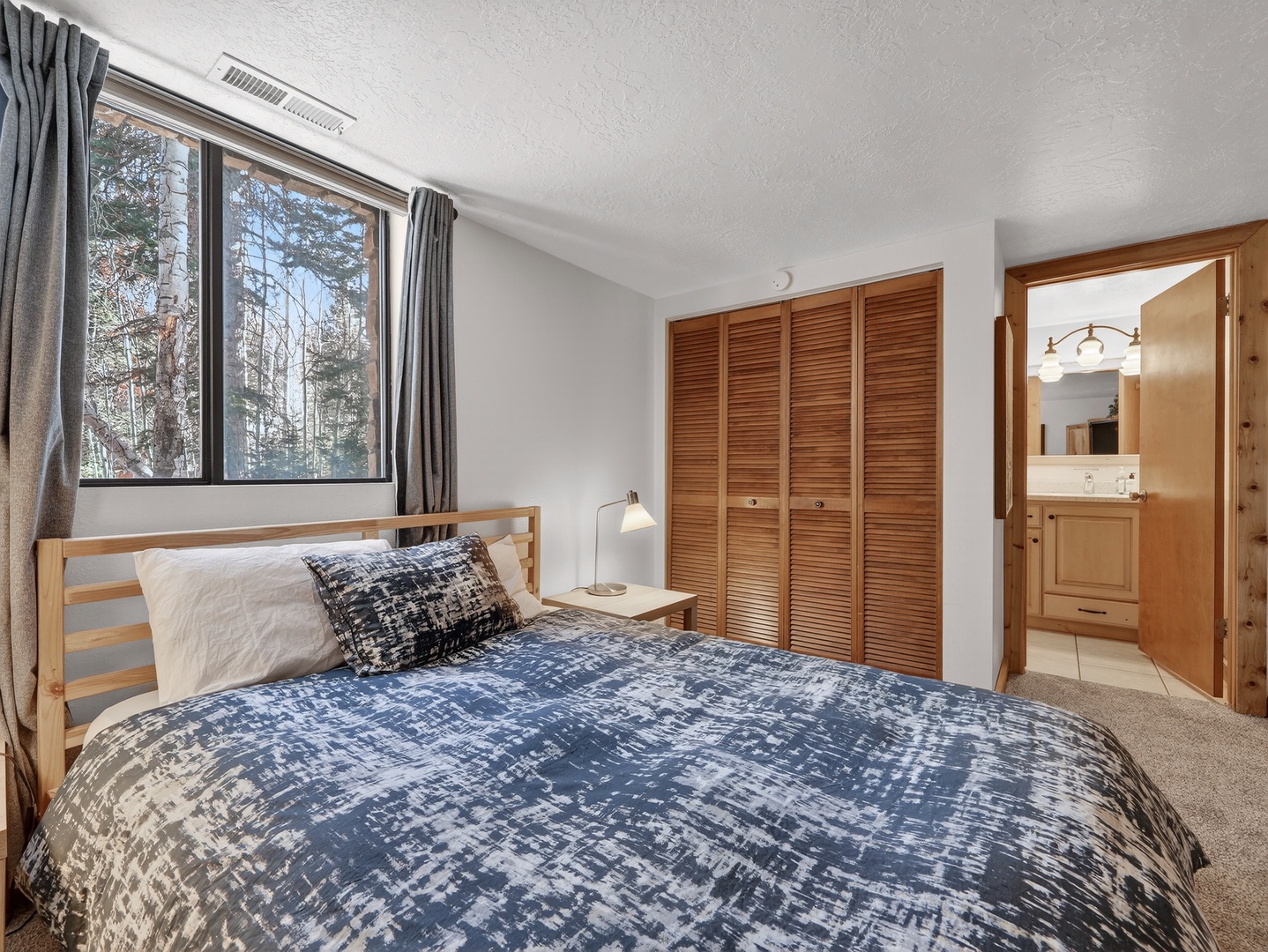 Wake up in this cozy bedroom with forest views through large windows. Your private space features comfortable bedding and warm wood accents.
