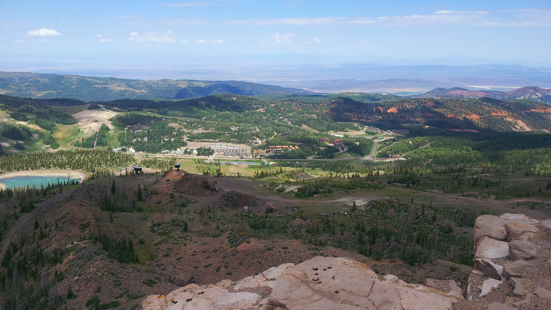 Aerial view showcasing the property's stunning mountain location, surrounded by expansive forests, rolling hills, and distant peaks under a clear blue sky.