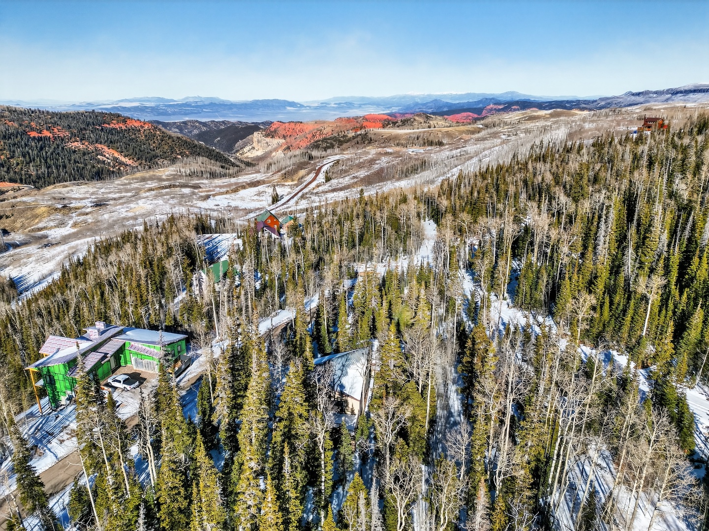 Aerial view showcasing the property nestled among snow-dusted evergreens with stunning mountain vistas and colorful canyon formations in the distance.