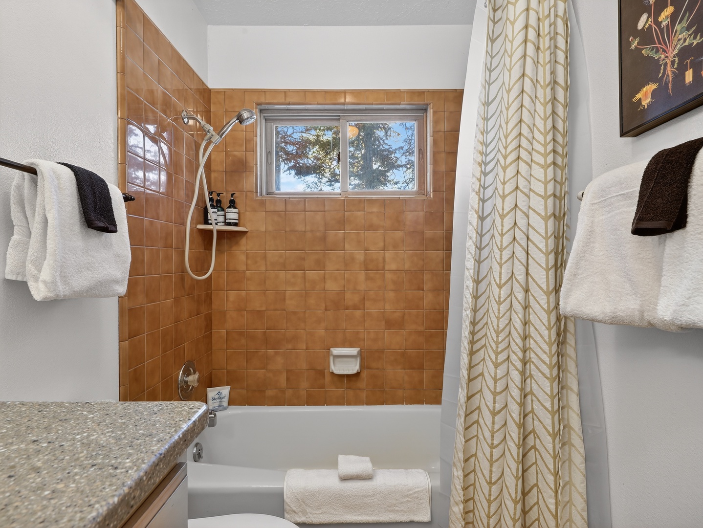 Refresh in your private tub/shower combo featuring warm tile surrounds, fluffy towels, and peaceful tree views through the window.