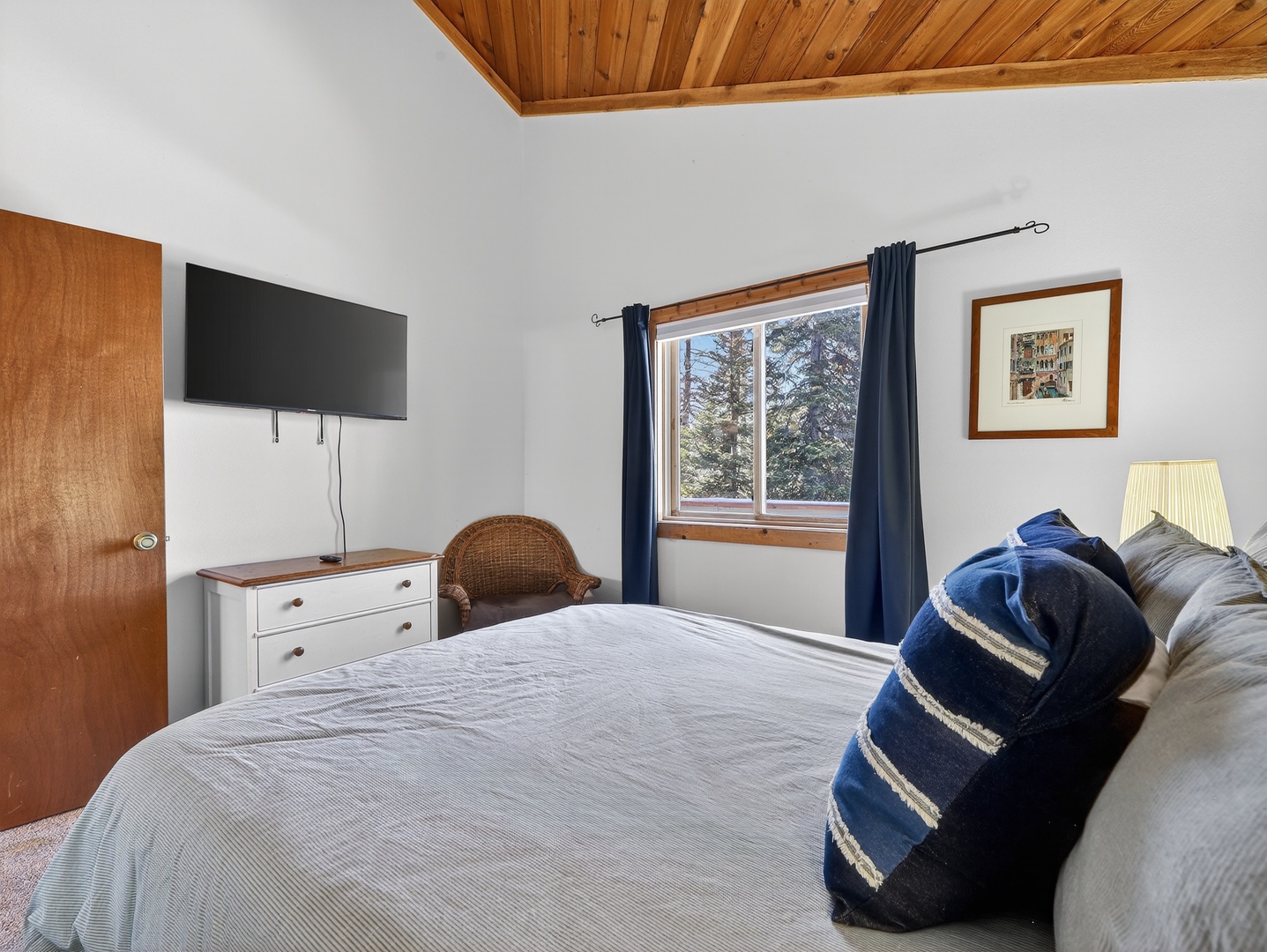 Relax in your cozy bedroom with warm wood ceiling, flat-screen TV, and peaceful forest views through your window.