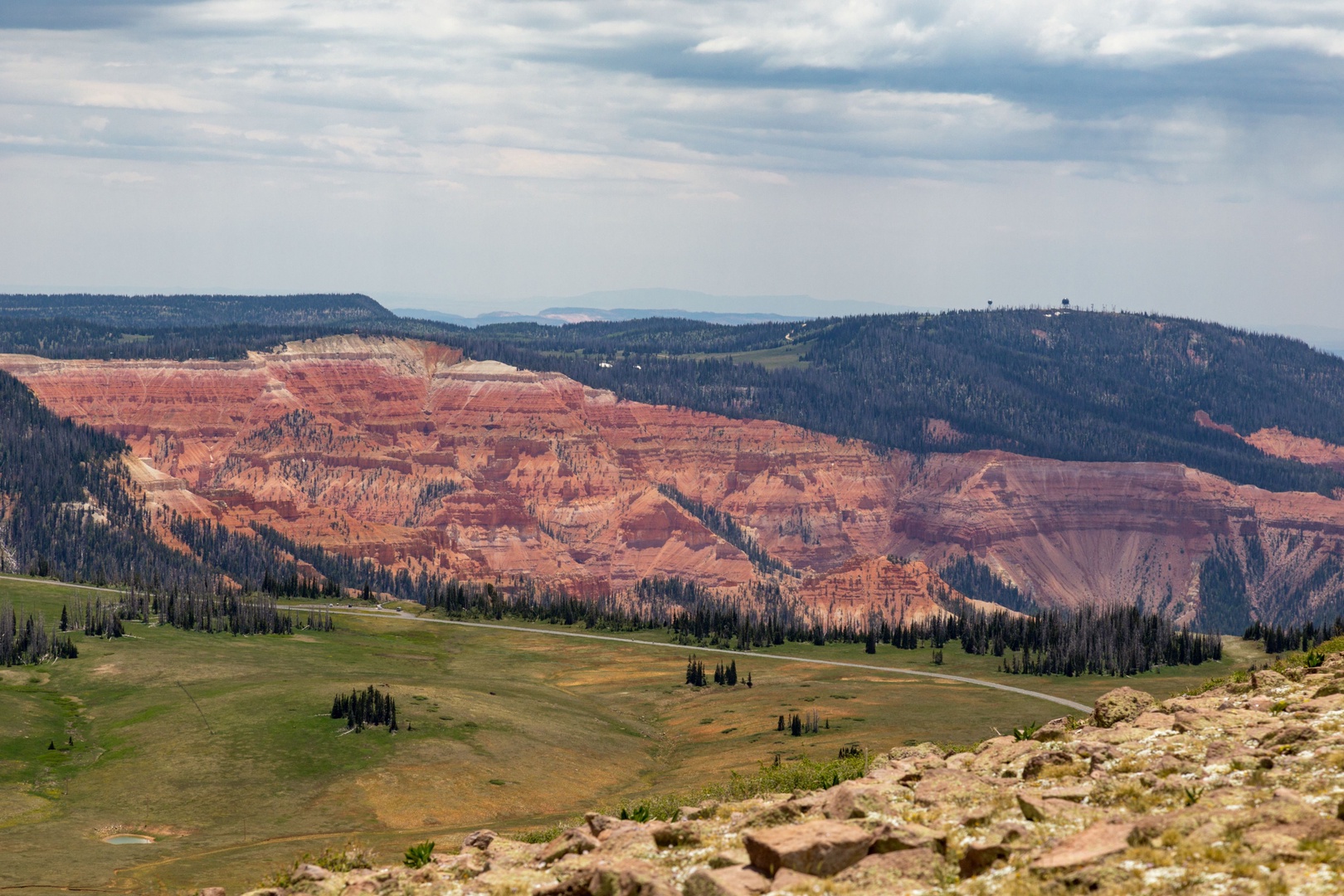 Stunning natural landscape with dramatic red rock formations, rolling meadows, and forested ridges under a sweeping sky near the property.
