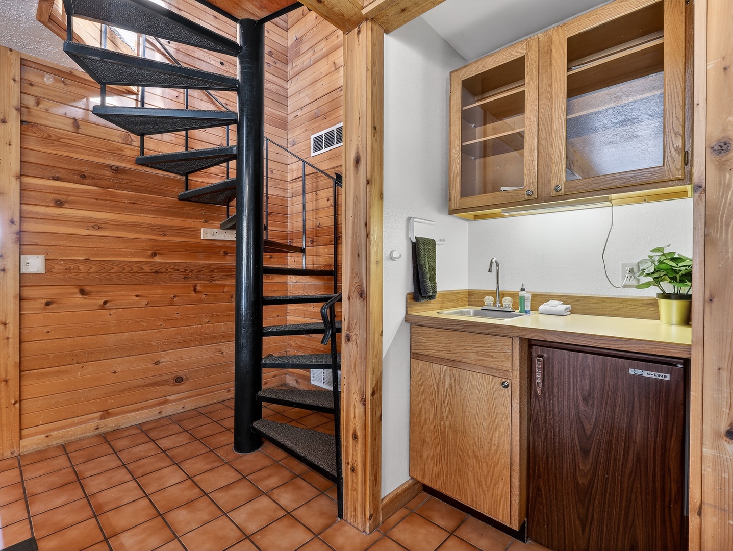 Your charming kitchen blends rustic wood charm with modern convenience, featuring warm timber cabinets and a spiral staircase leading to your loft retreat.