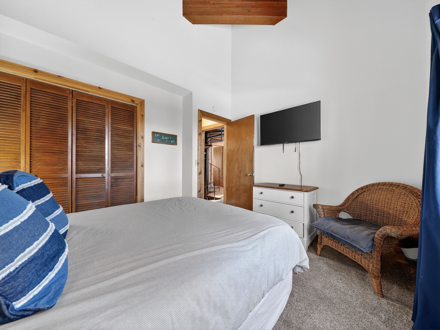 Relax in your serene bedroom with coastal charm, featuring a comfy bed, wicker seating, and wall-mounted TV for cozy evenings.