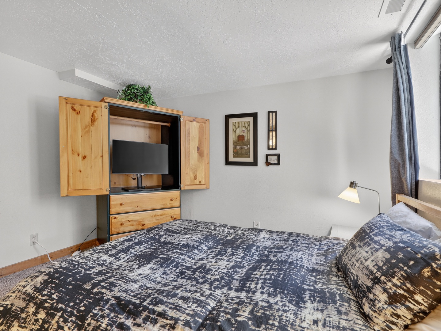 Relax in your cozy bedroom featuring a comfortable bed, charming wooden entertainment center, and thoughtful touches that make you feel right at home.