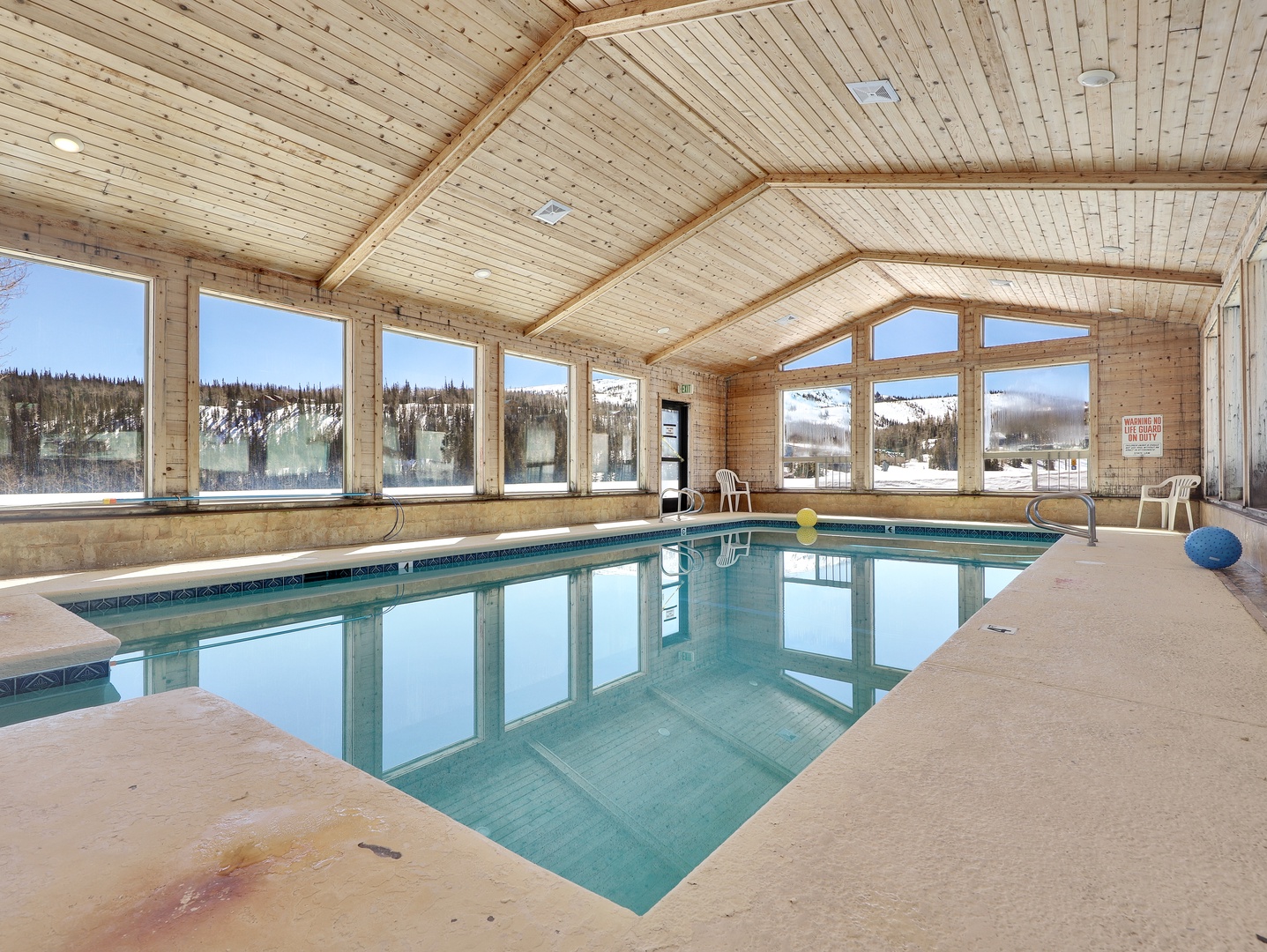 Dive into your private heated pool with soaring vaulted ceilings and breathtaking mountain views through floor-to-ceiling windows, perfect for year-round relaxation in every season.