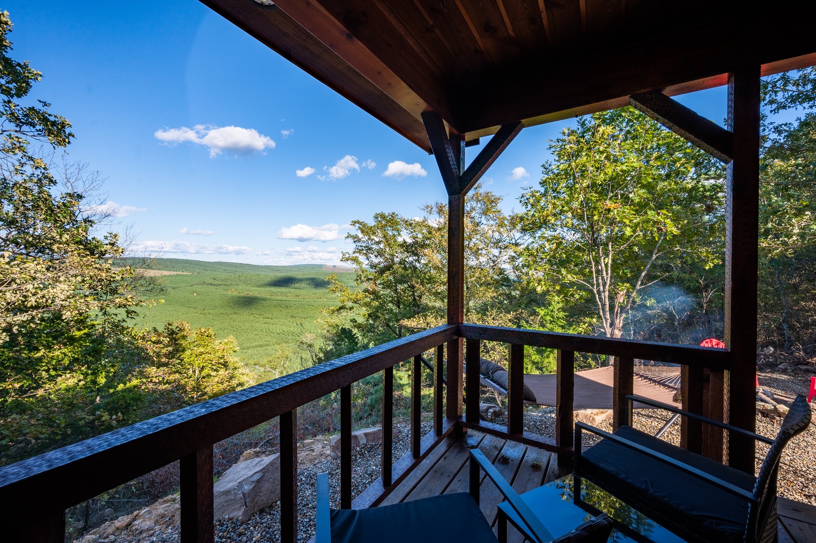Expansive mountain views stretch across rolling green hills from this covered balcony, where wooden beams frame the natural landscape perfectly.