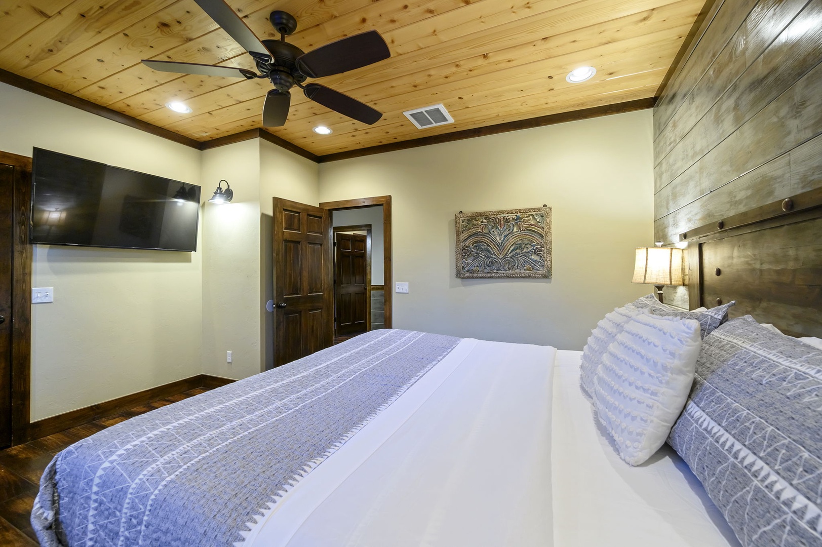 Step into your cozy bedroom with rustic wood-paneled ceilings, a plush king bed, and warm lighting. The ceiling fan keeps you comfortable while the mounted TV and decorative touches make this space your perfect retreat.