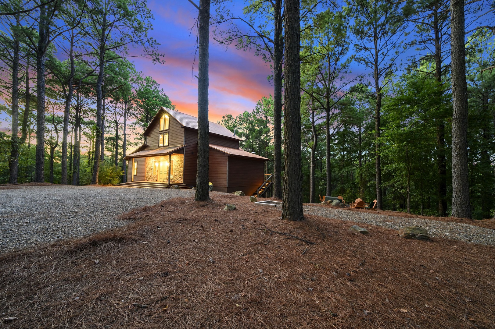 A secluded modern cabin nestled among tall pines, lit warmly against a stunning sunset sky. The private forest setting offers tranquil surroundings and ample parking for your peaceful retreat.
