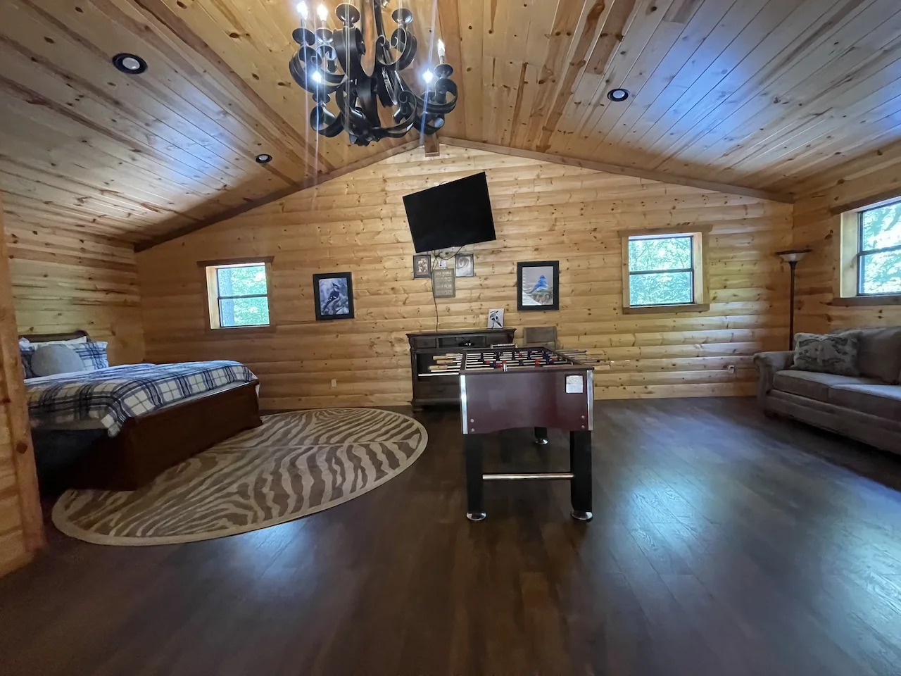 Your cozy cabin retreat features vaulted ceilings with warm wood paneling, a plush sleeping area, a comfortable sofa, and a foosball table for fun—perfect for unwinding after exploring.