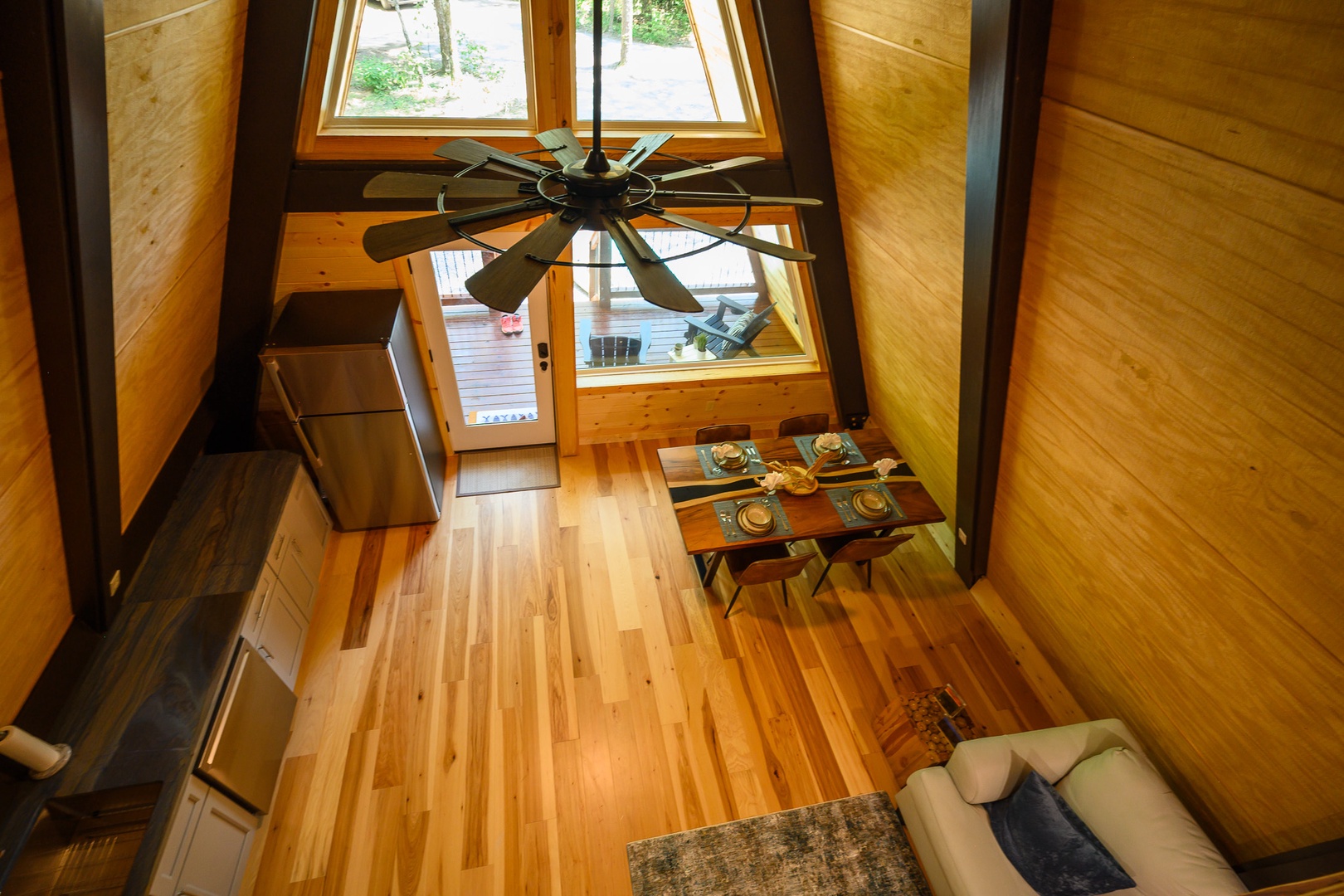 Step into your airy A-frame retreat where soaring wood-beamed ceilings and floor-to-ceiling windows flood the space with natural light, creating a warm and inviting atmosphere for your getaway.