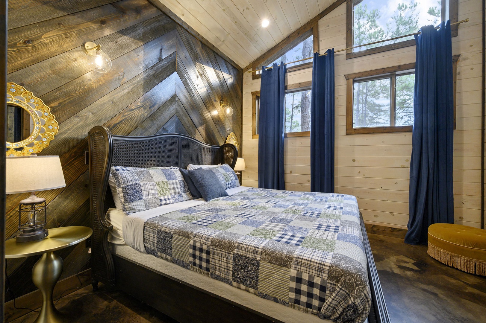 Slip into your cozy retreat under a cathedral ceiling of reclaimed wood, where natural light streams through tall windows framing peaceful forest views. Your plush bed awaits beneath soft, rustic beams.