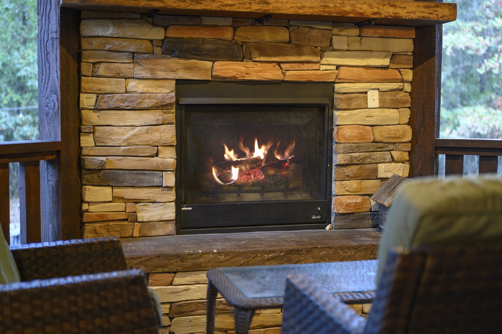 Gather around your private stone fireplace with flames crackling behind the glass, set against a backdrop of peaceful forest views through the deck windows.