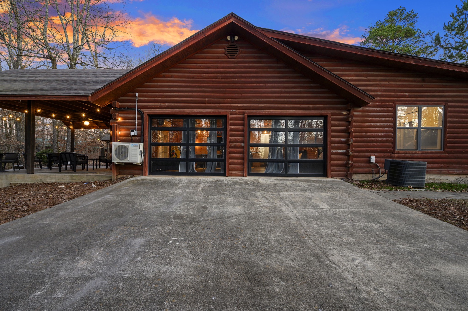 Beautiful log cabin with spacious driveway and covered patio area, surrounded by natural wooded setting during golden hour.