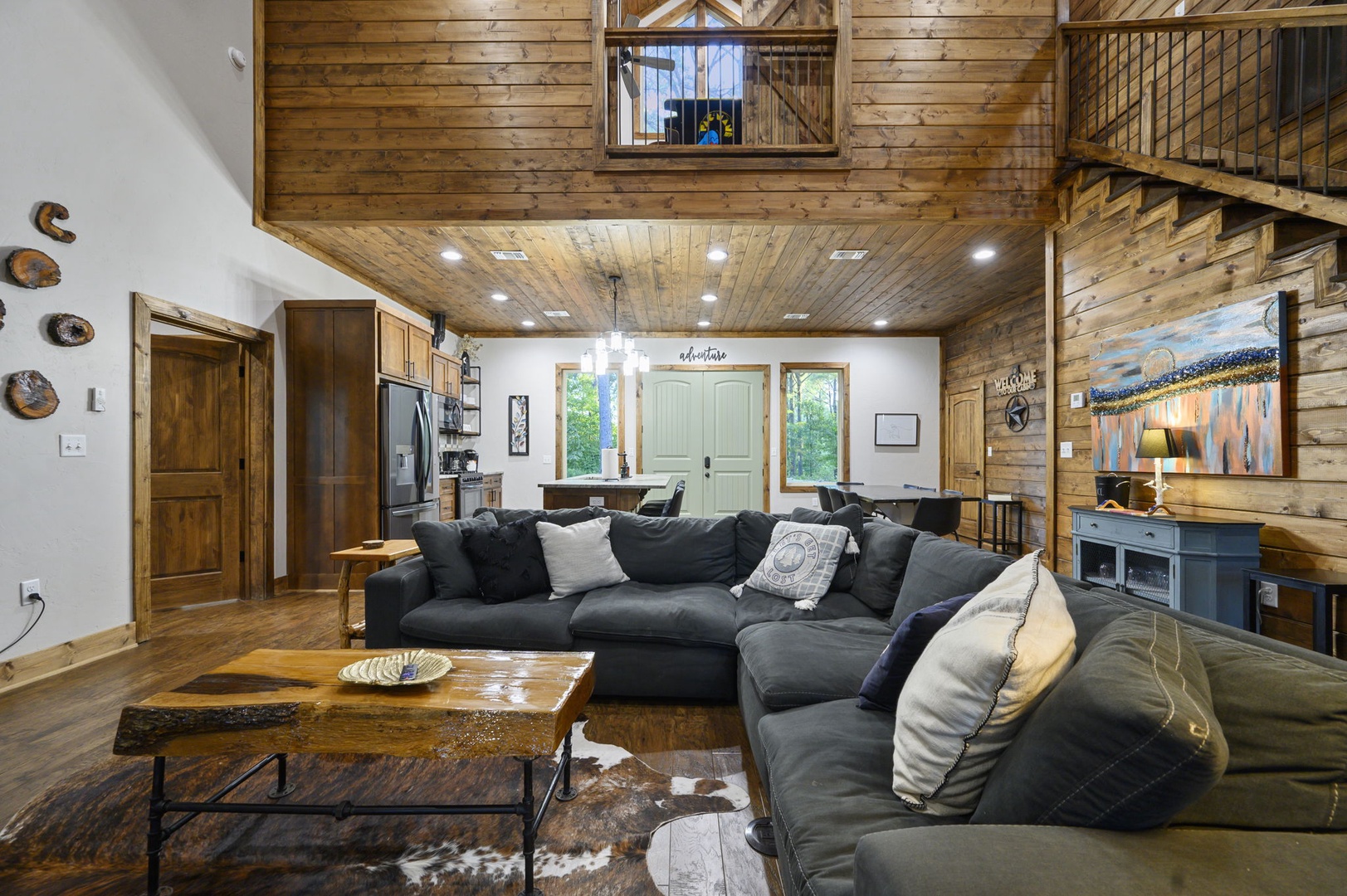Settle into your spacious living area with soaring wood-beamed ceilings, plush sectional seating, and natural light streaming through the loft above—perfect for gathering and unwinding together.