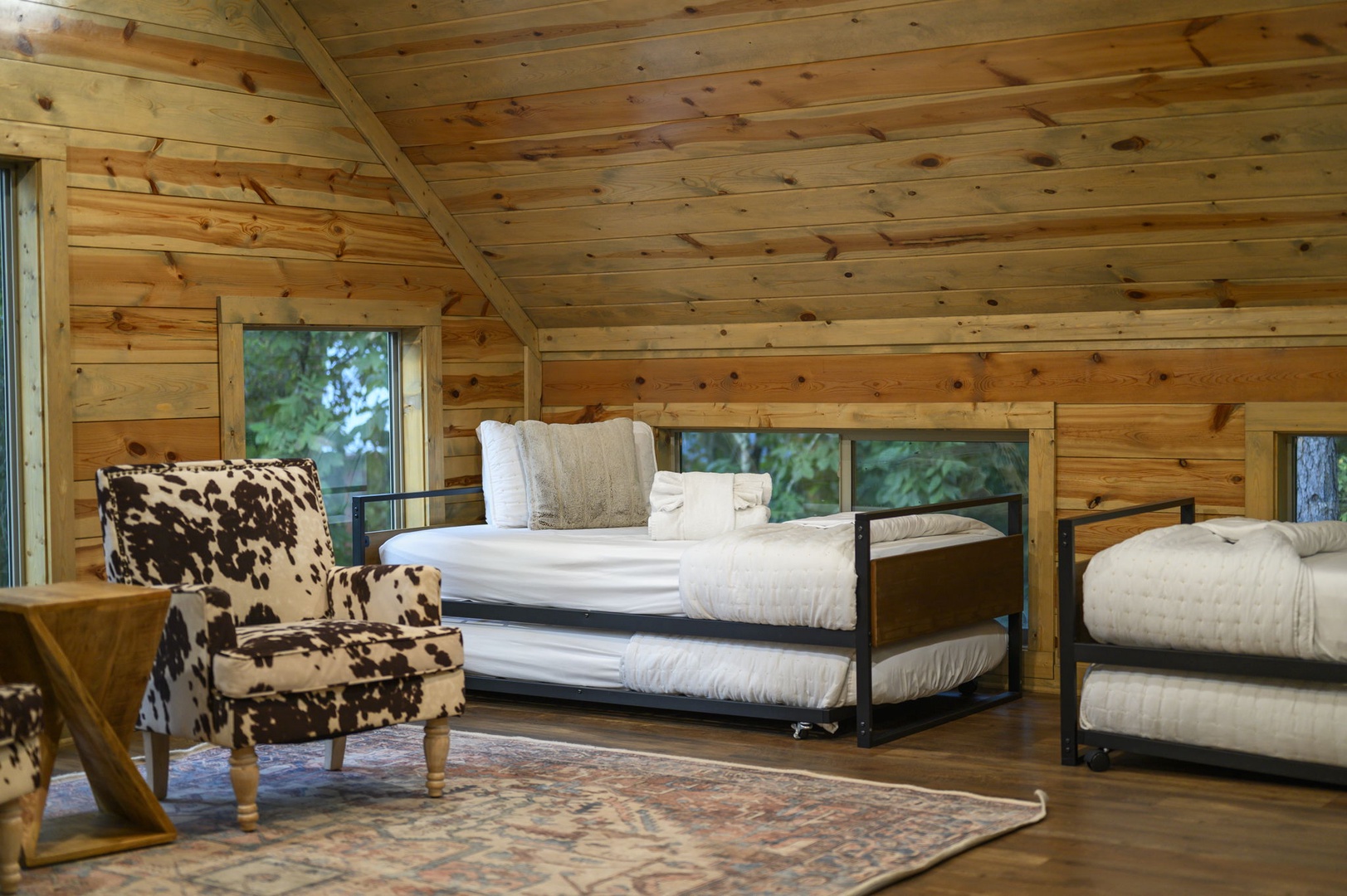 Unwind in your cozy loft retreat, where rustic pine walls meet plush bedding and natural forest views. Sink into the stylish accent chair and let the peaceful woodland setting wash over you.