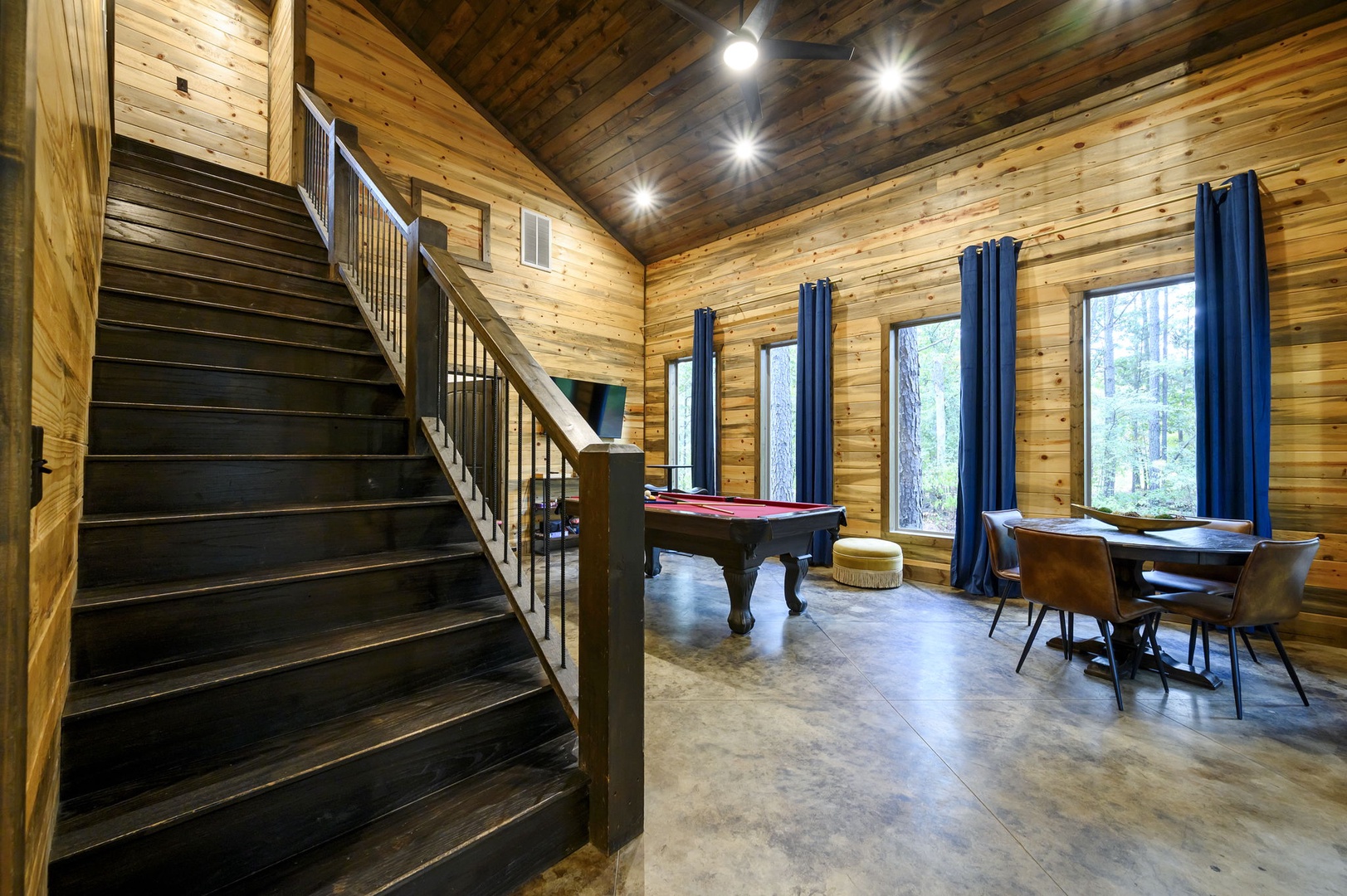 Step into your rustic retreat with soaring wood-beamed ceilings and abundant natural light. Gather around the game table for cards and conversation, or challenge friends to pool, all framed by towering trees outside.