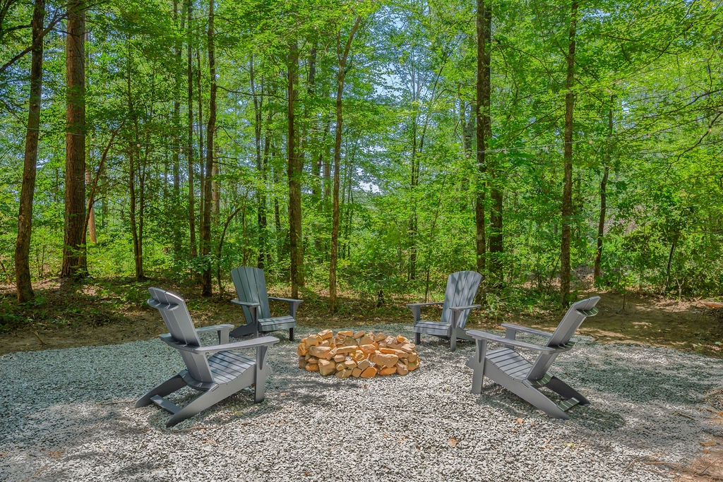 Your private woodland retreat features a stone fire pit encircled by Adirondack chairs—perfect for evening gatherings under a canopy of towering trees.