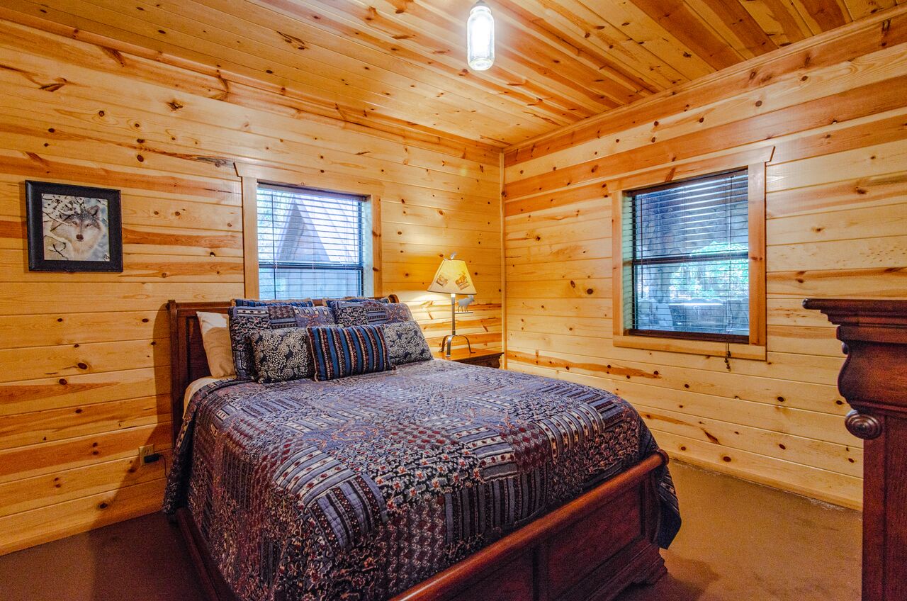 Slip into your cozy cabin retreat where warm pine walls and a plush quilt create the perfect mountain escape. Natural light streams through windows, inviting you to unwind in this peaceful bedroom.
