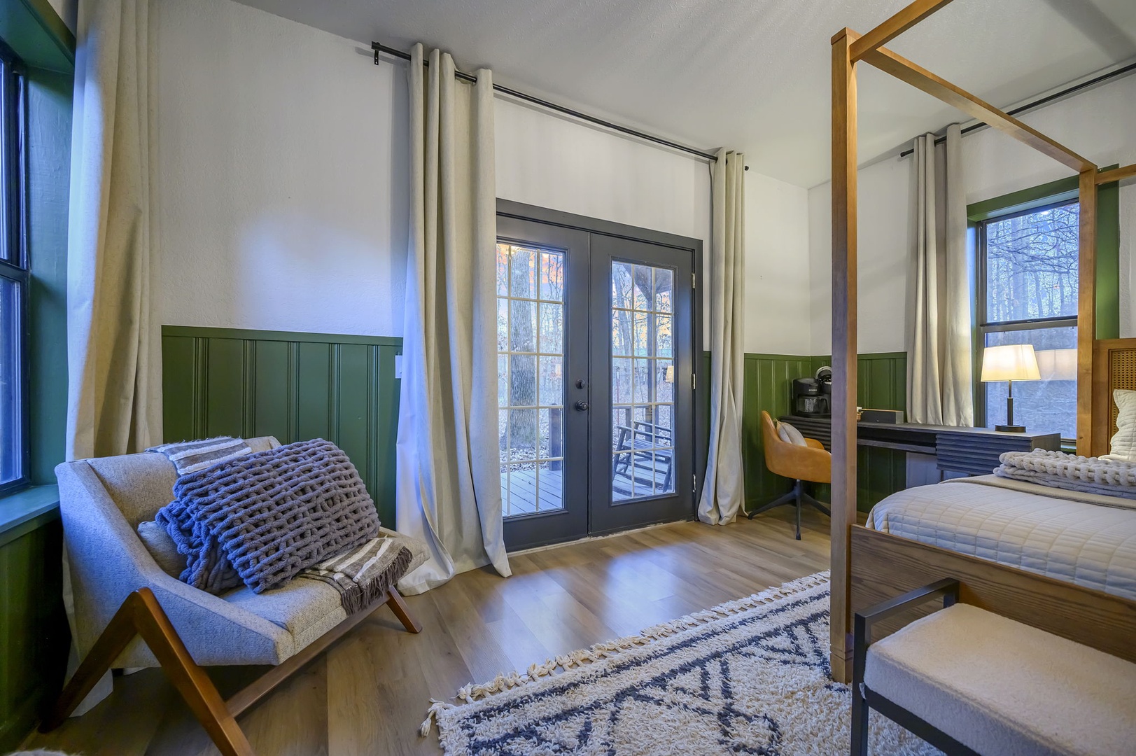 Unwind in your stylish bedroom featuring a cozy four-poster bed, modern chair, and French doors opening to your private outdoor space.