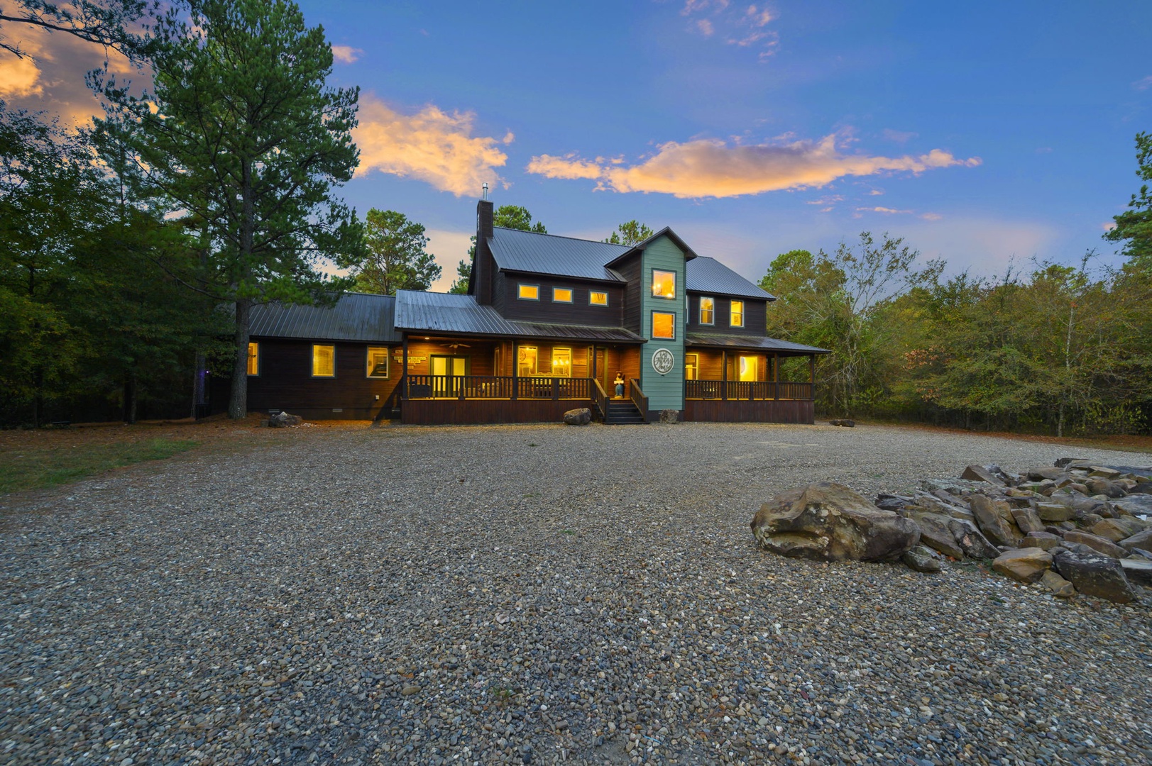 A charming retreat nestled among towering pines, glowing warmly against a stunning twilight sky and surrounded by serene natural landscape.