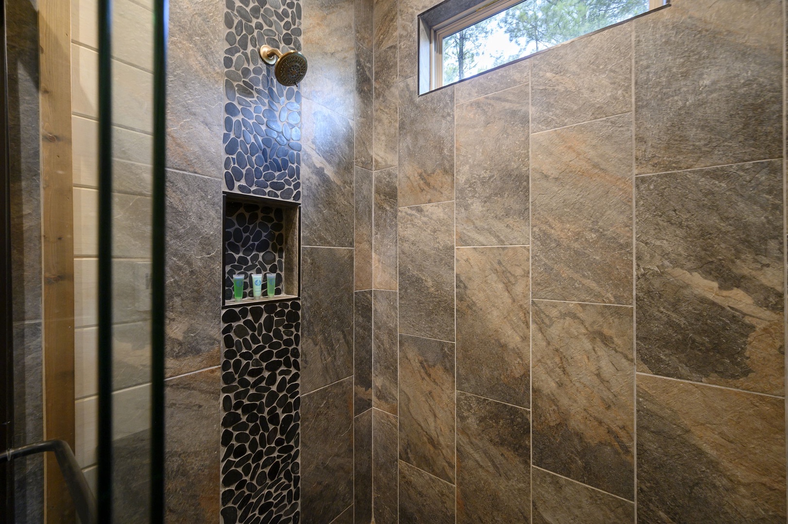 Step into your luxurious walk-in shower with soothing stone-look tile and a stylish pebble-accent niche. Natural light streams in from above, making each rinse feel like a refreshing escape.