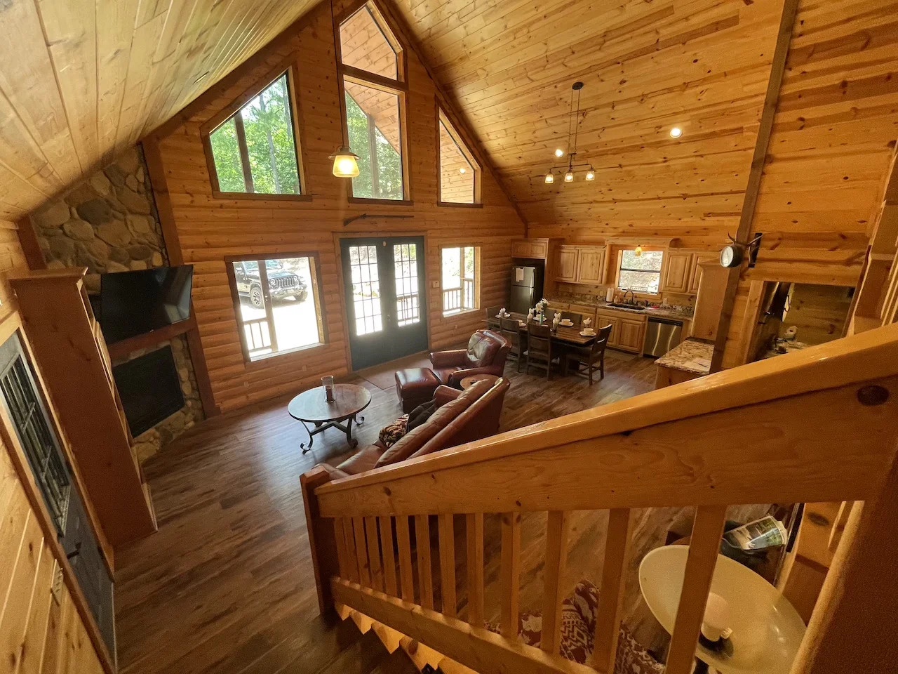 Step into your cozy cabin retreat where warm wood wraps around you, vaulted ceilings soar, and natural light pours through tall windows. Sink into the leather sofa by the stone fire or gather at the dining table—your perfect mountain escape awaits.