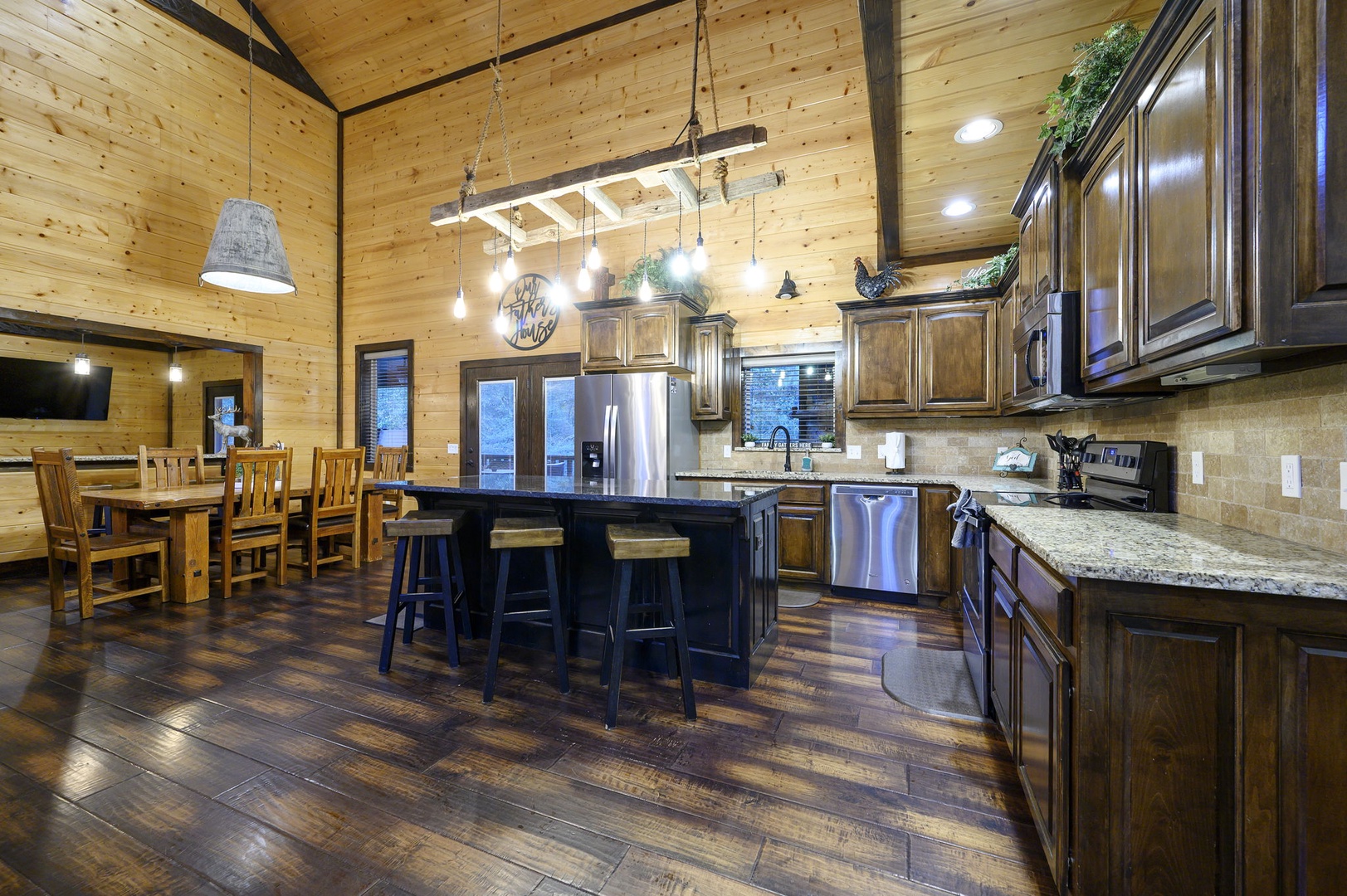 Gather around the spacious kitchen island for meal prep or morning coffee, then share stories at the rustic dining table under warm, glowing lights. Rich wood tones and modern appliances blend for effortless comfort.