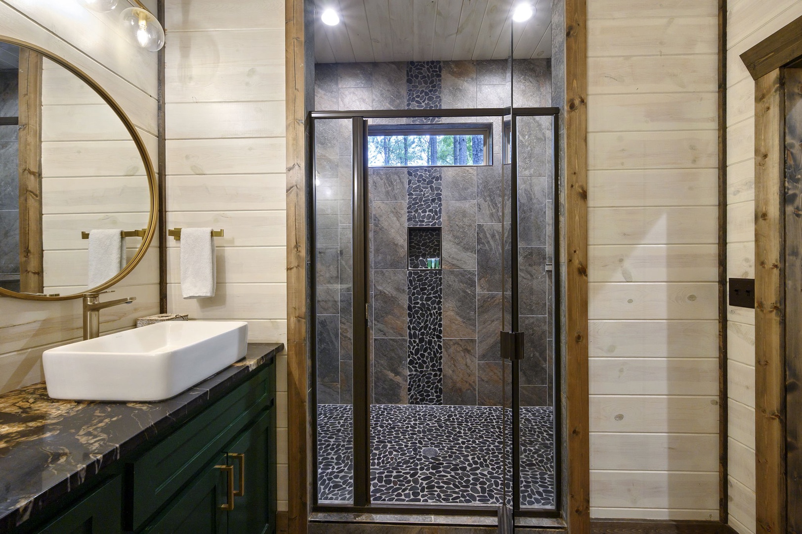 Your private spa-like retreat awaits, complete with a stunning walk-in shower framed by natural light, elegant finishes, and peaceful forest views through the window.